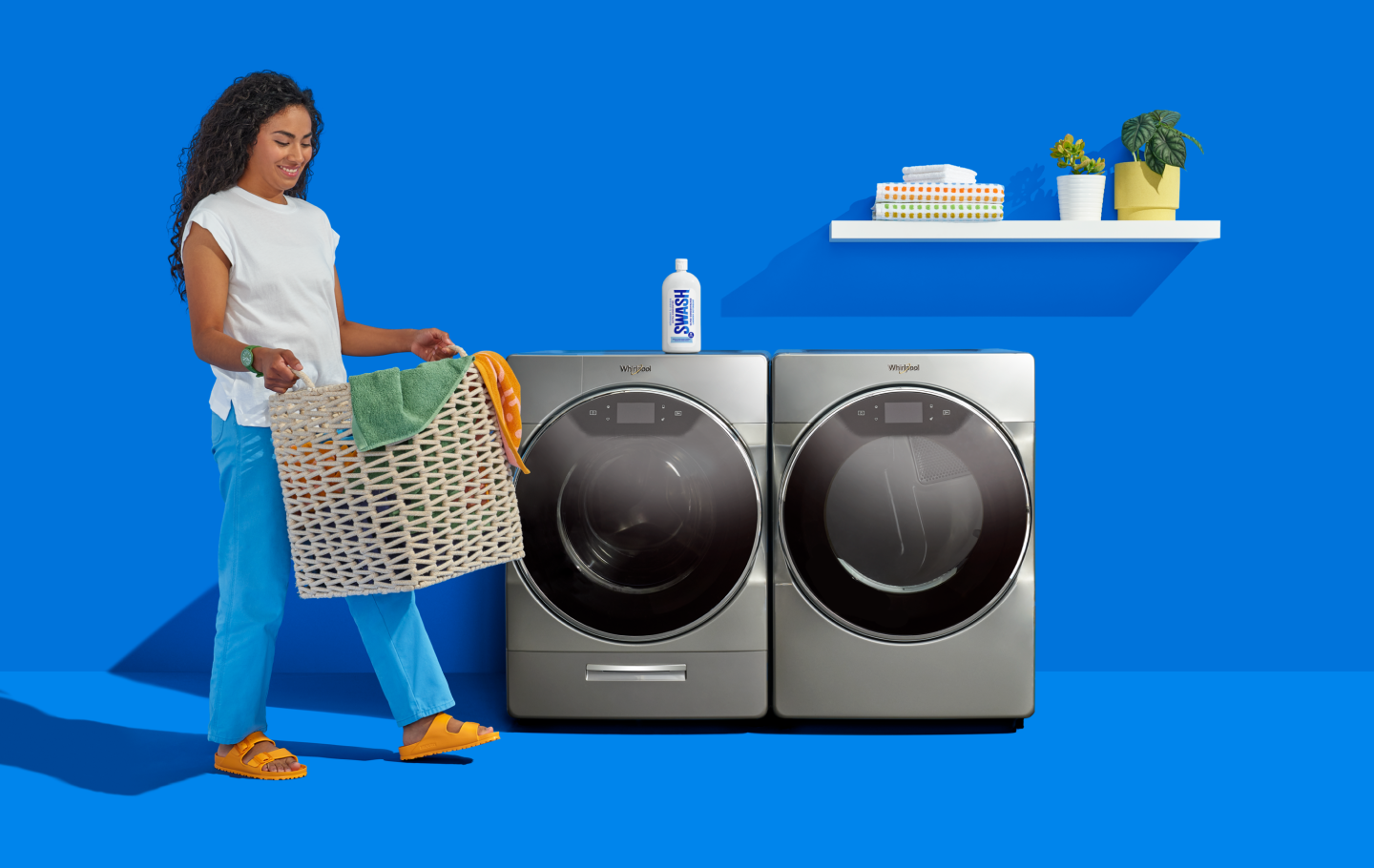 A woman carrying a laundry basket infront of a Whirlpool® front load washer and dry.