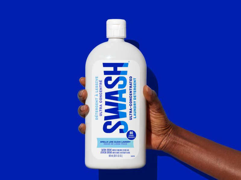 A hand holding a bottle of Swash® Smells Like Clean Laundry