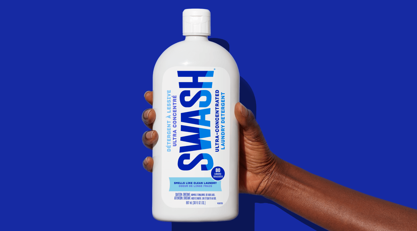 A hand holding a bottle of Swash® Smells Like Clean Laundry detergent.
