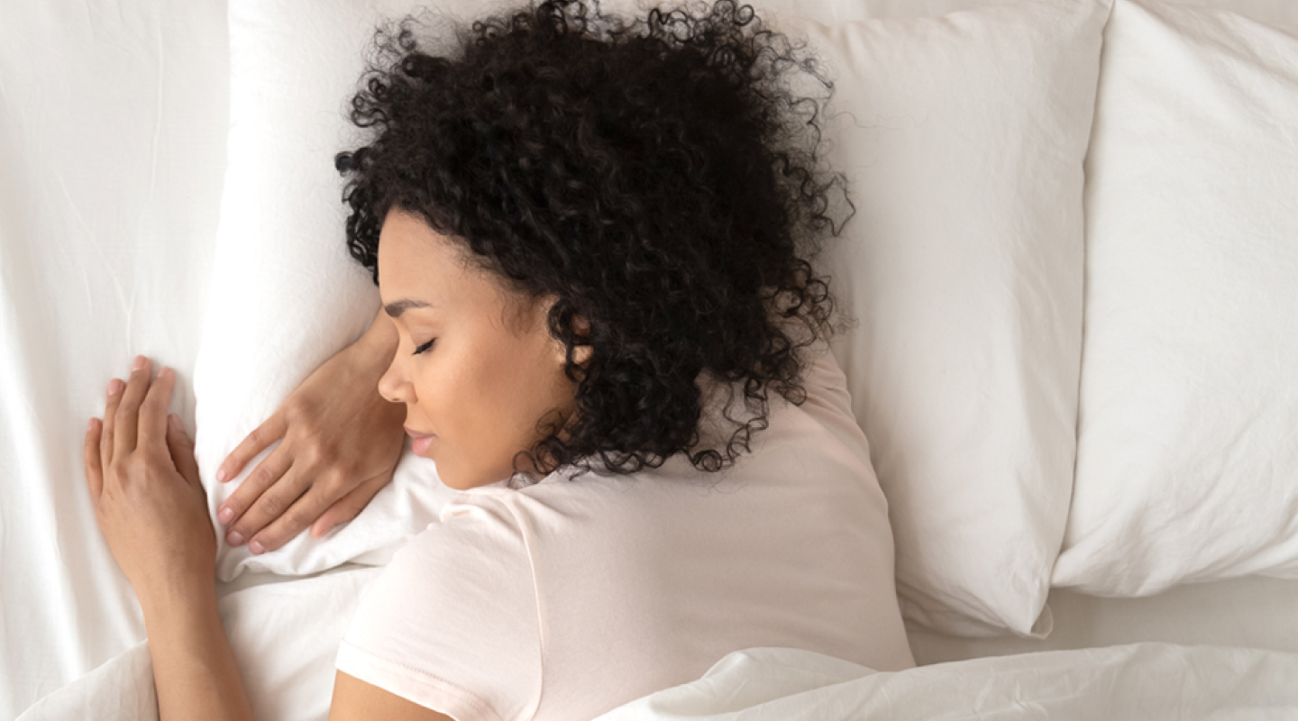A woman sleeps on clean, white sheets with her head on a fresh pillow.