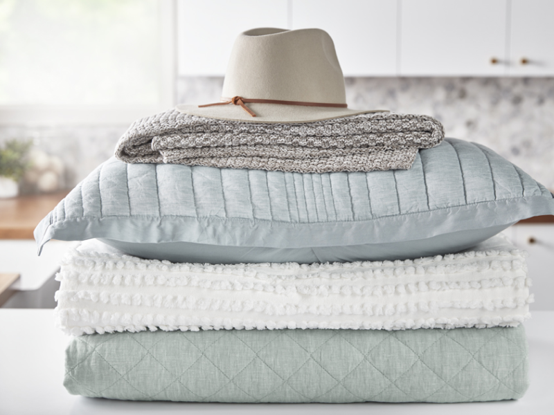 A stack of blankets, pillows and a hat sit on a laundry room counter.