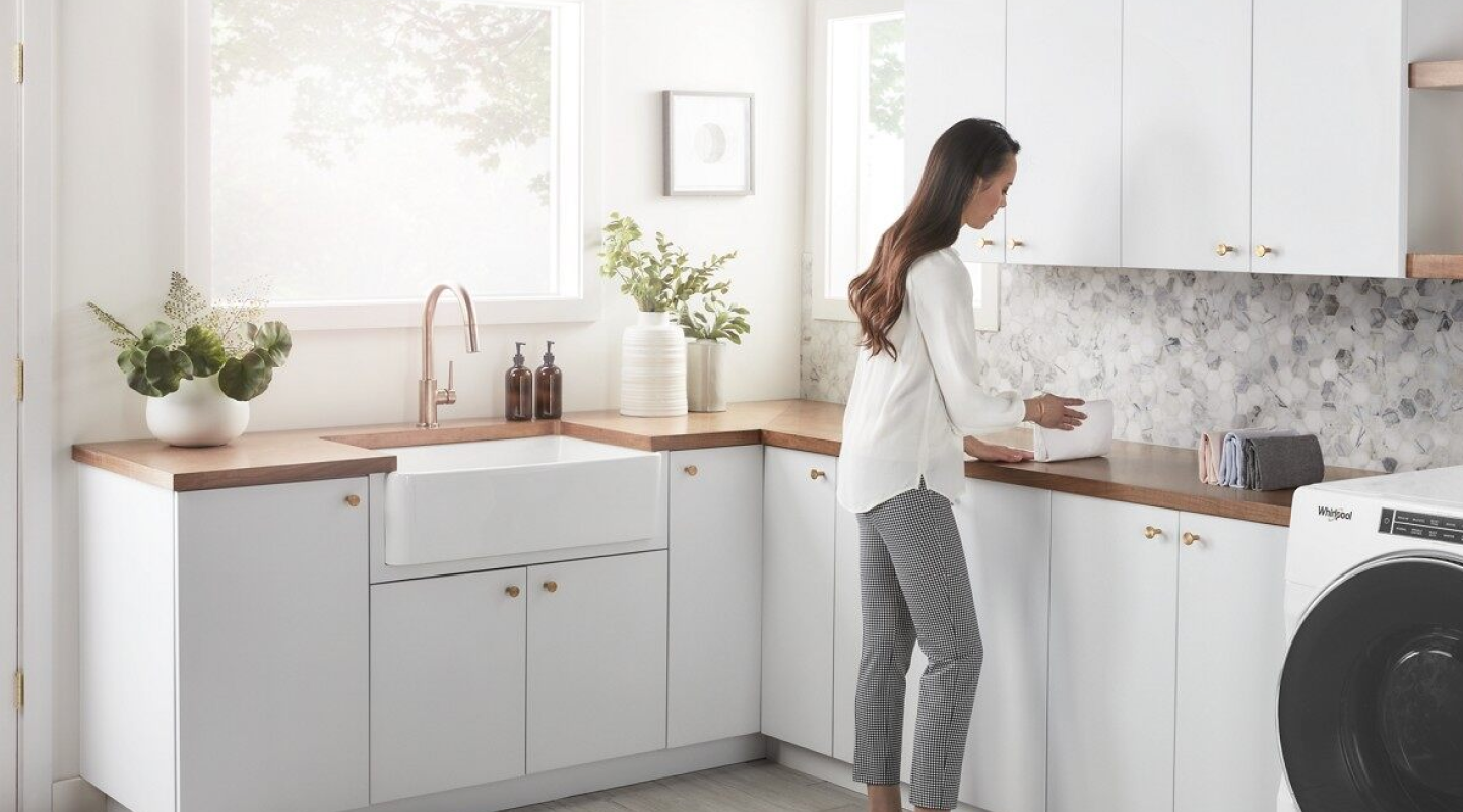 A woman in a white blouse folding her laundry in her laundry room.