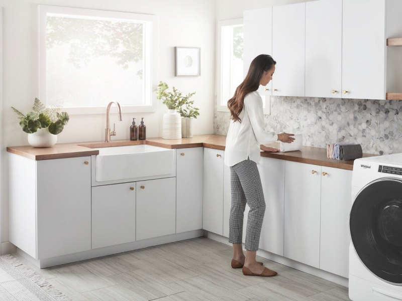 A woman in a white blouse folding her laundry in her laundry room.